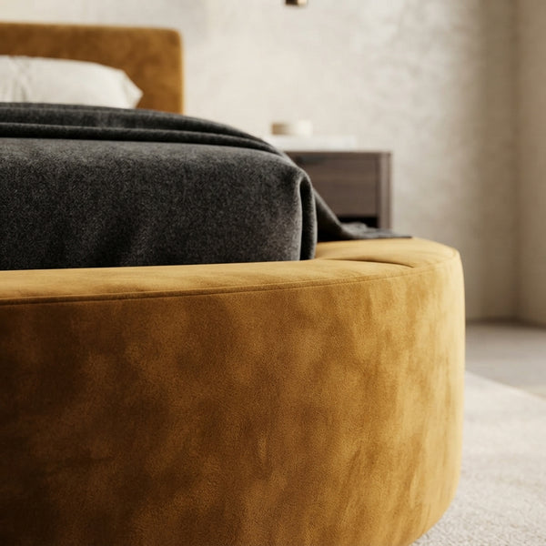 Close-up view of high-density deep ochre velvet fabric on a rounded bed frame in a modern, neutral bedroom.